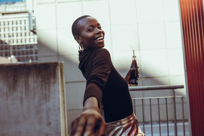 Happy young African woman leaning against a rail with soft drink