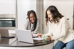 Two women talking together at the kitchen table and working on a laptop