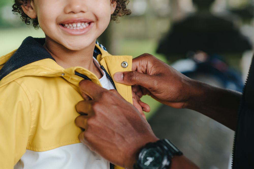 Cropped image of parent closing jacket for a smiling boy