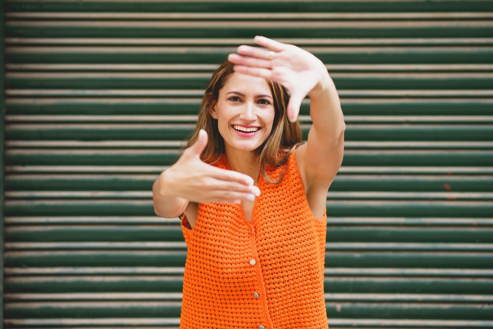 Portrait of woman smiling at camera framing her face with hands