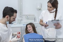 Male dentist showing dental jaw model to female patient in dentist's office 42azy5