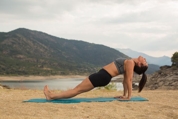 Woman practicing yoga outdoors near water