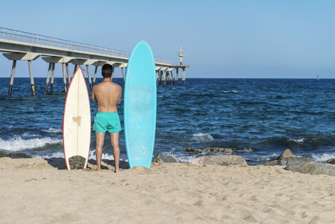 Male surfer standing with two boards and looking out to the coast
