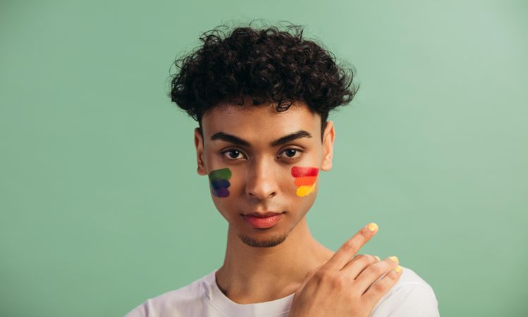 Portrait of a young man with rainbow flag painted on his cheeks.