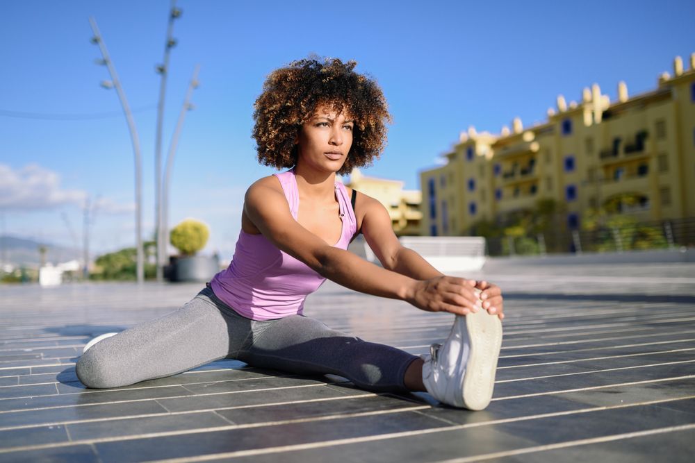 Female with afro warming up with cityscape in the background