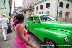 People walking down the street beside a green vintage car in Havana, Cuba bDM1y0