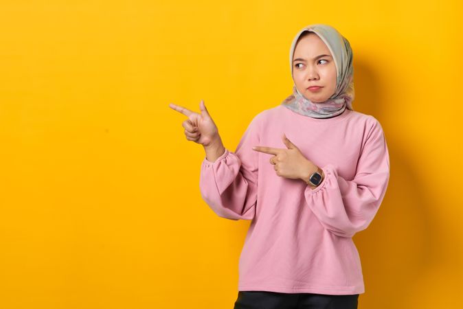 Serious Muslim woman in scarf pointing to her side