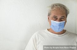 Portrait of middle aged man in light shirt wearing facemask against light wall 47q2B0