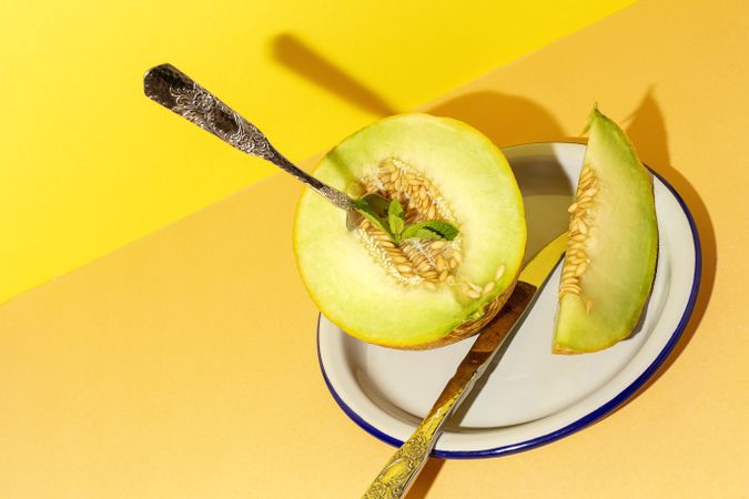Sliced small melon on plate with spoon and fork