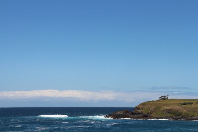 Scenic coastal view with rolling waves and clear blue skies near a grassy cliff in sunny weather