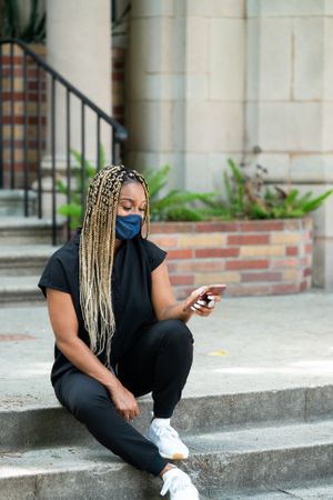 Medical worker sitting outside on steps checking messages on mobile phone