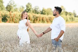 Cheerful expecting couple holding hands while bonding in field