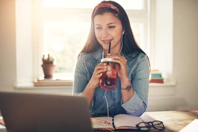 Woman working on laptop in home office sipping iced tea