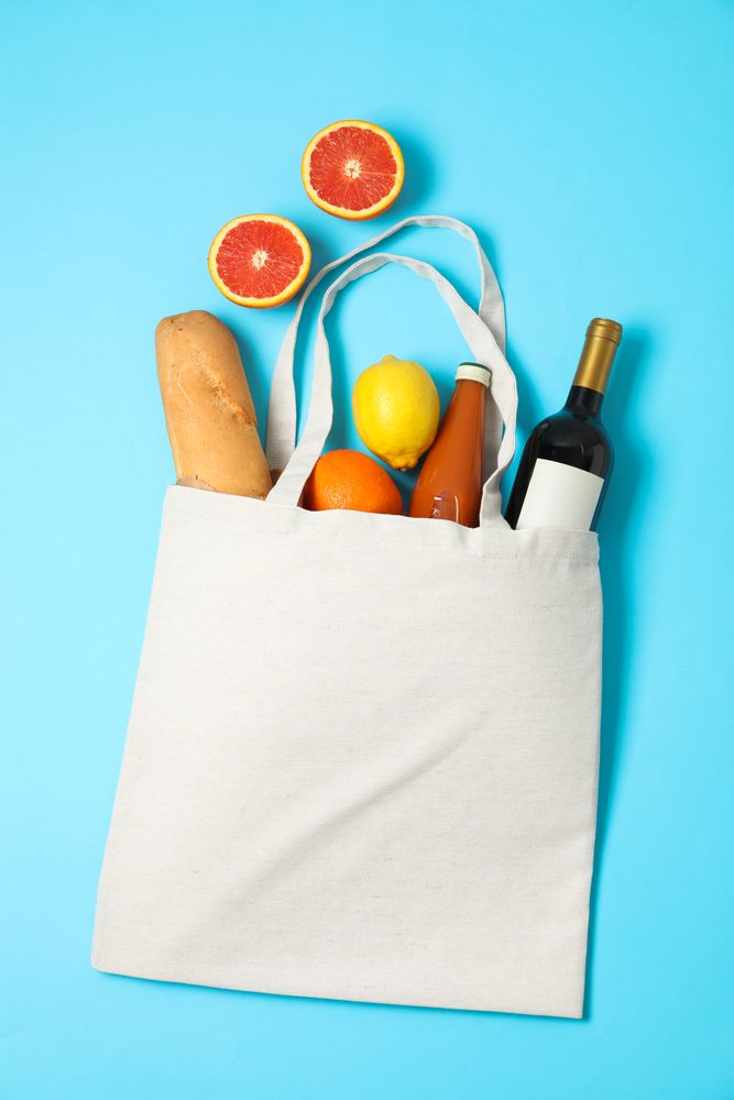 Eco bag with bottle of wine, juice, fruits and baguette on color background, space for text