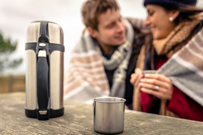 Flask of coffee on cold day with couple in background