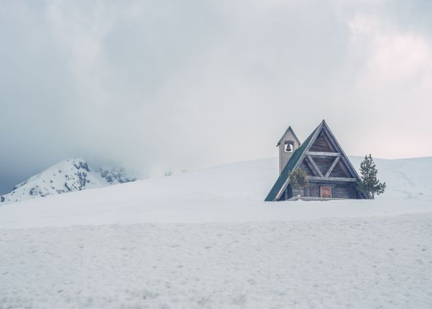 Wooden house with triangular roof located on snowy hill