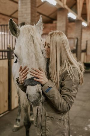 Woman hugging horse with long mane in face in stable