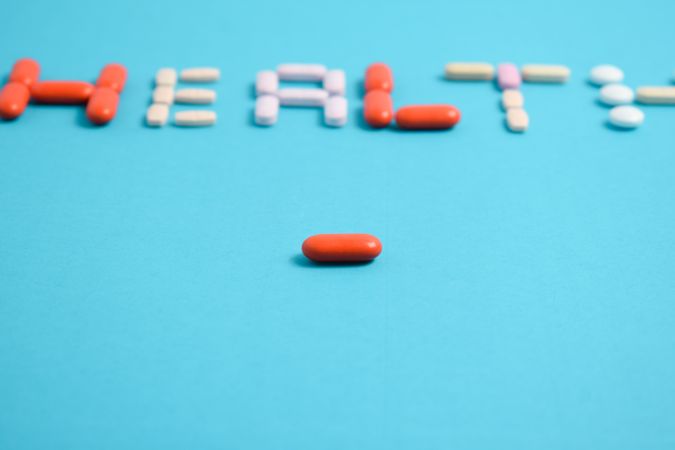 Pills spelling the word "HEALTH" on blue background with copy space