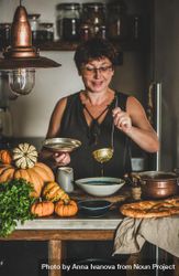 Woman with short hair and glasses with soup ladle in kitchen in cozy kitchen bxjYd5