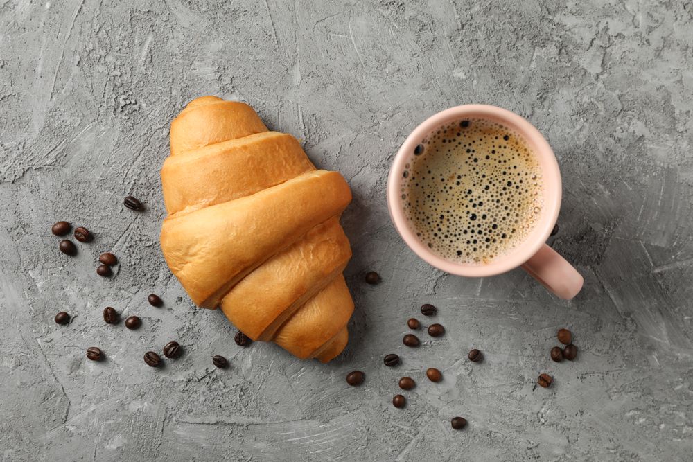 Croissant and pink mug of coffee on grey table, top view