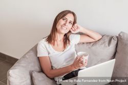 Woman thinking on sofa with a cup of coffee working on her laptop in the morning 0PDna0