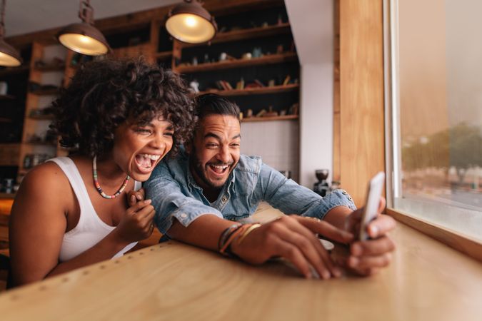 Young man and woman laughing while taking selfie in cafe