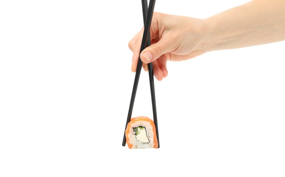 Female hand with chopsticks holds sushi roll, isolated on plain background