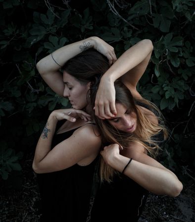 Young women posing near green bush