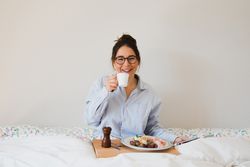 Young woman with breakfast on bed using smart phone