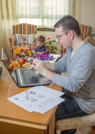 Father working in home office and son playing
