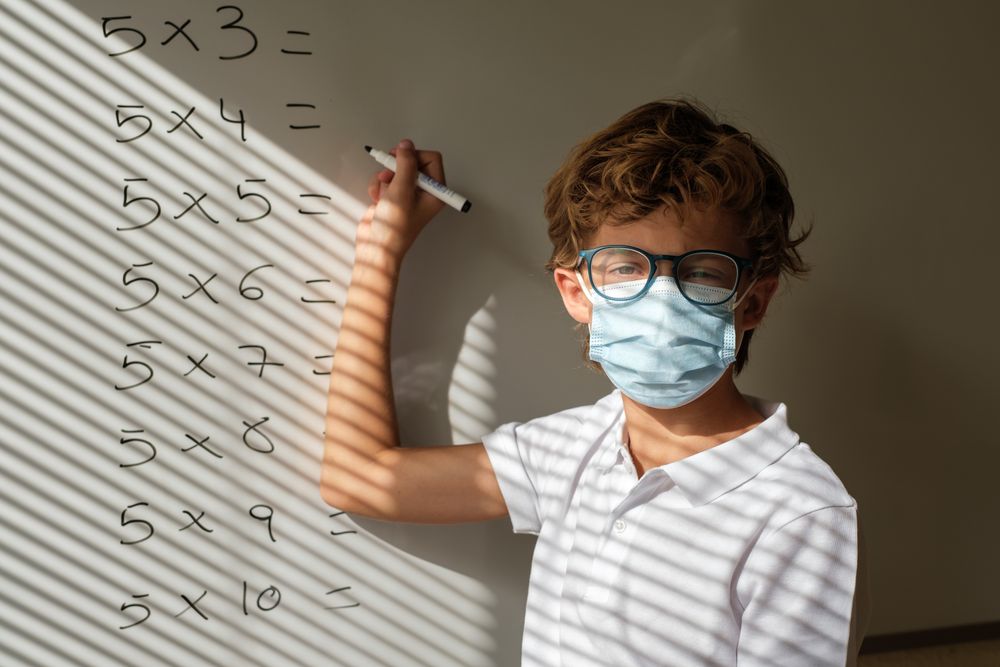 Schoolboy in mask writing on whiteboard during math lesson