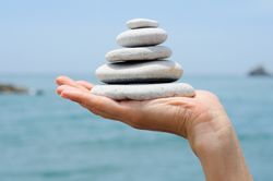 Side view of hand with small pile of rocks with ocean in background