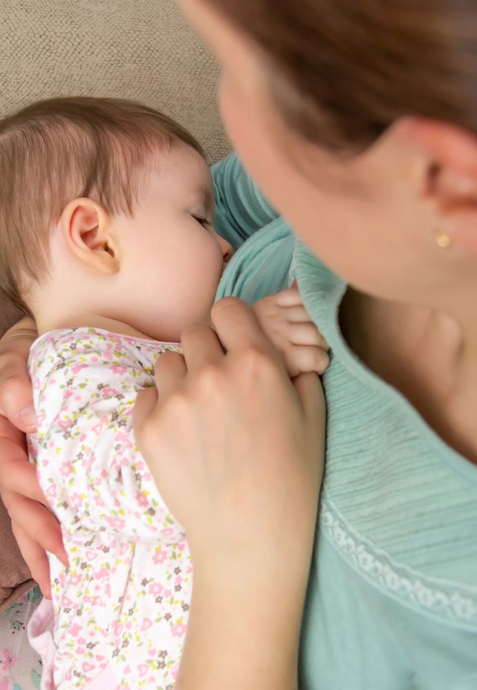 Close up of baby girl breastfeeding with mother, vertical