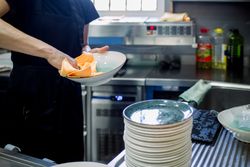 Crop woman in apron wiping plates in kitchen