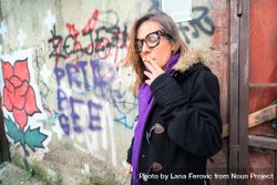 Woman in glasses smoking next to grafitti 0PAVv5