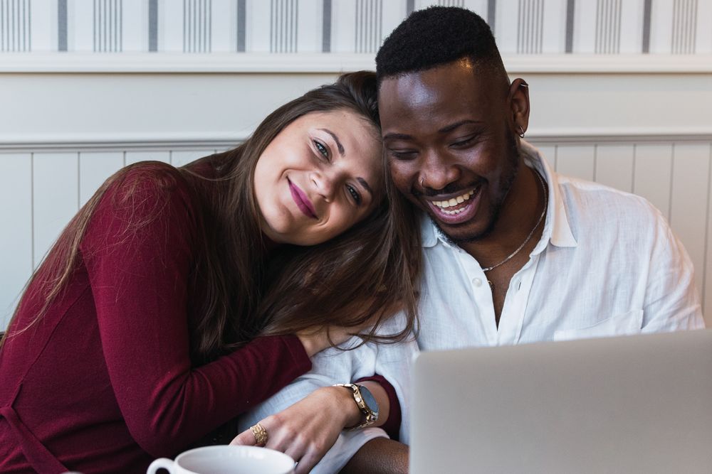 Cheerful multiethnic couple using laptop during breakfast at home
