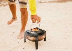 Tanned man cooking on camping stove beside parked mini van
