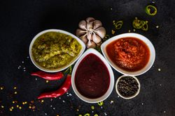 Top view of flavorful spicy traditional Georgian sauces on dark counter with garlic and chilis