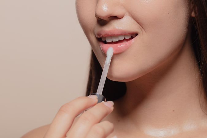 Close up of young Korean woman applying transparent lip gloss