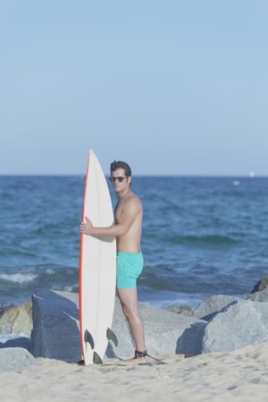 Male surfer standing on rock near sea with board