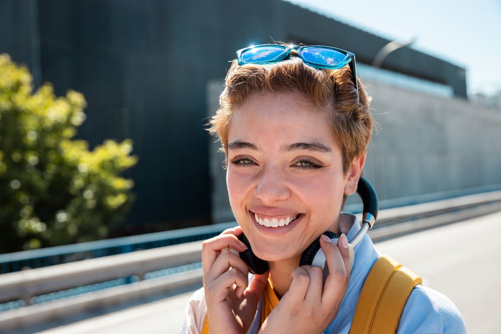 Playful trendy woman on street in sunshine covering camera with hands