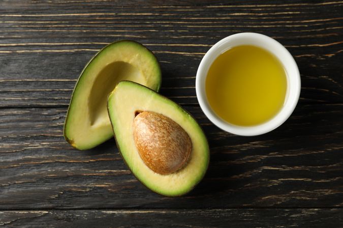 Ripe fresh avocado and oil on wooden background, top view