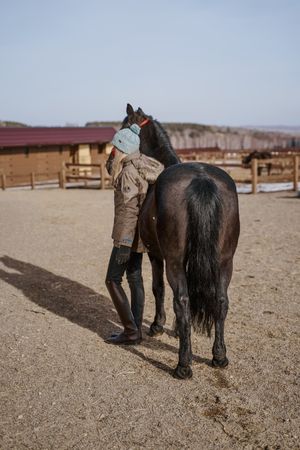 Warm dressed woman with brown horse by hay