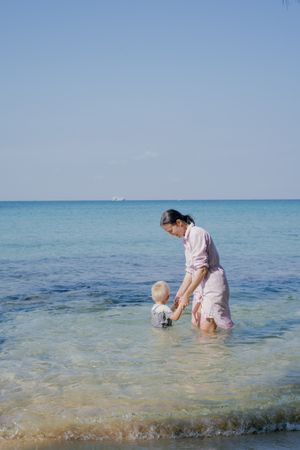 Woman and small kid having fun with water while relaxing on seacoast at resort