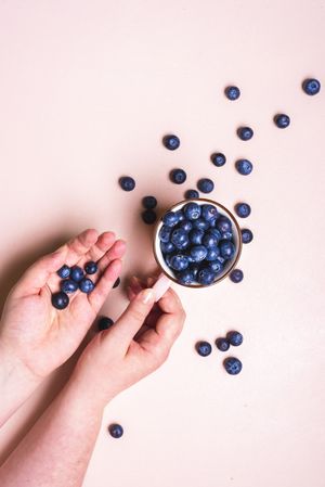 Fresh blueberry fruits in a cup top view with fresh blueberries in a woman's hands