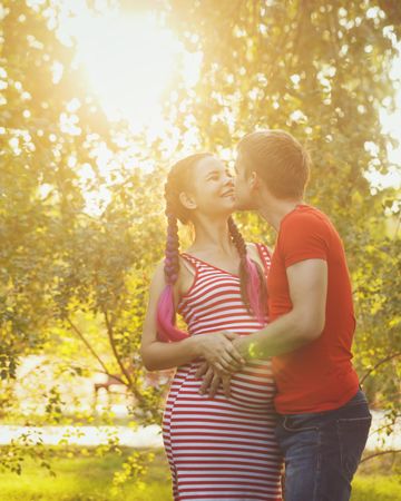 Pregnant woman her partner embracing in sunny park