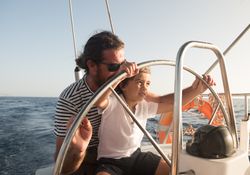 Man and boy holding steering wheel on yacht on water