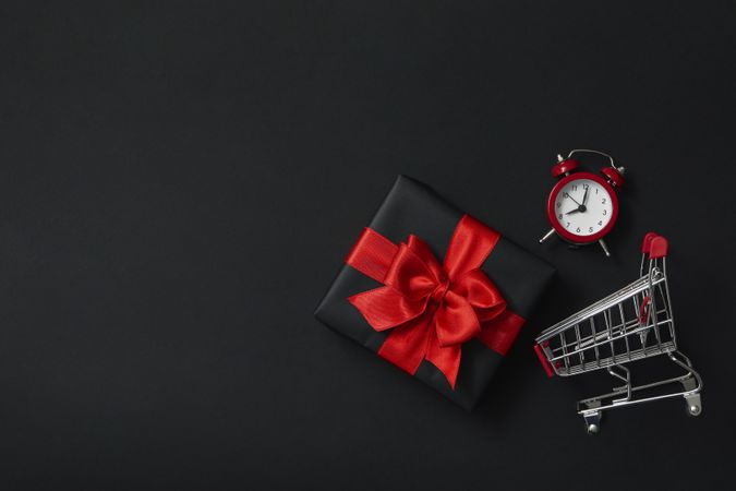 Gift box, alarm clock and shop trolley on dark background