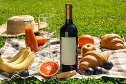 Bottle of wine, croissants, fruits, straw hat and towel on grass, space for text