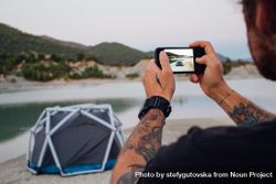 Man taking picture of tent set up on lake 5rM1p0